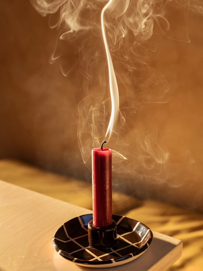 Ceramic Patterned Candlestick Holder, a colourful candlestick holder sitting on a table stop surface. It is accompanied by a recently lit candle. 