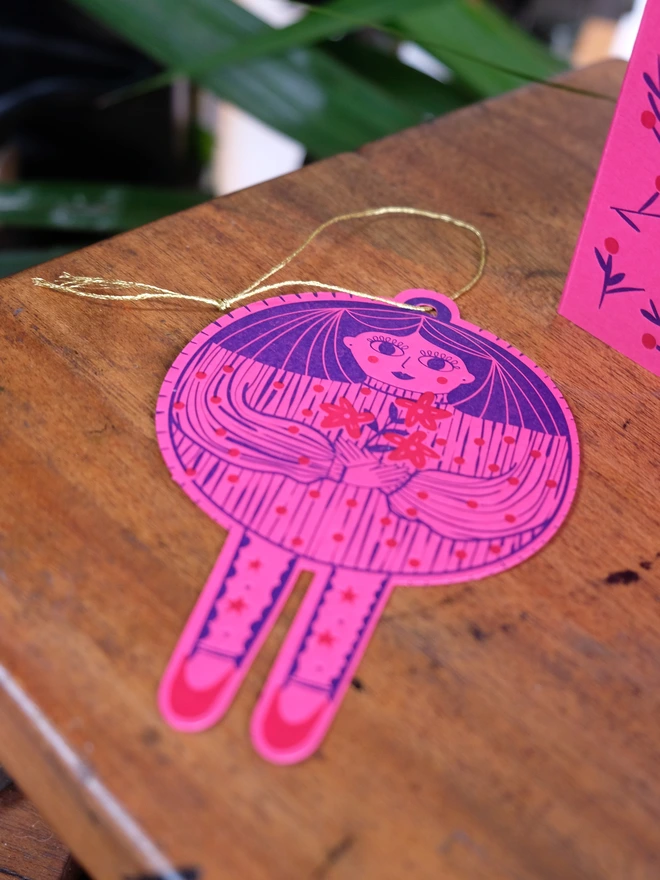 Blue and red handprinted babule lady, a festive pop-out Christmas card. Decoration laying on the table with string. 