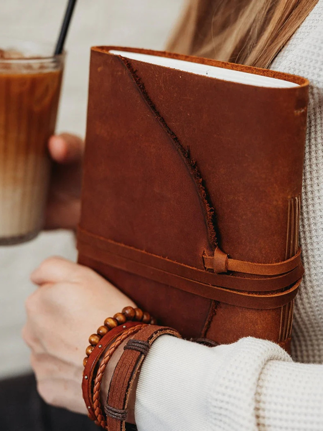 leather bullet journal. a dark brown leather journal in one hand, an iced latte in the other.