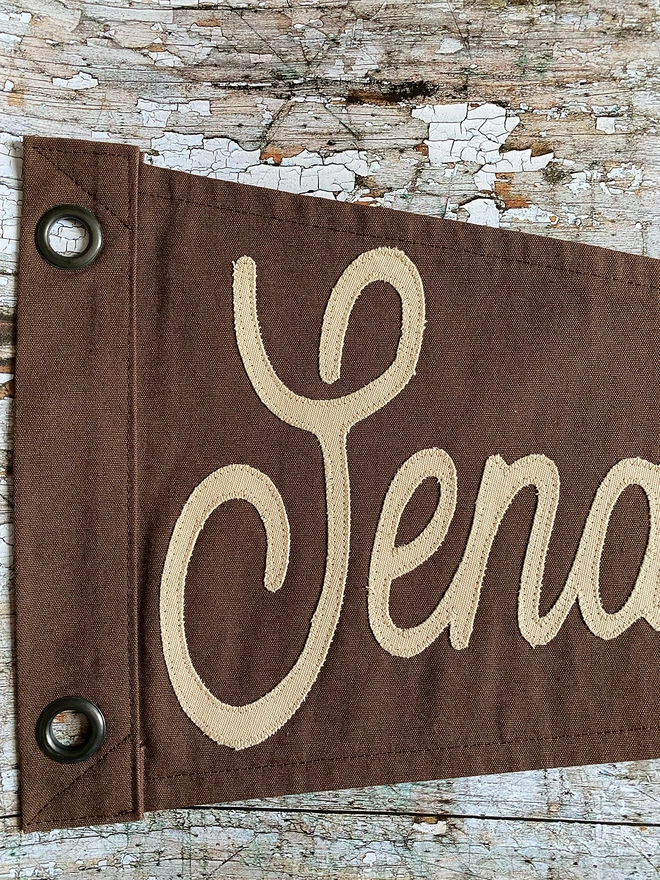 Detail of an espresso brown 'Send Coffee' pennant flag showing the word Send in a ;latte coloured canvas.