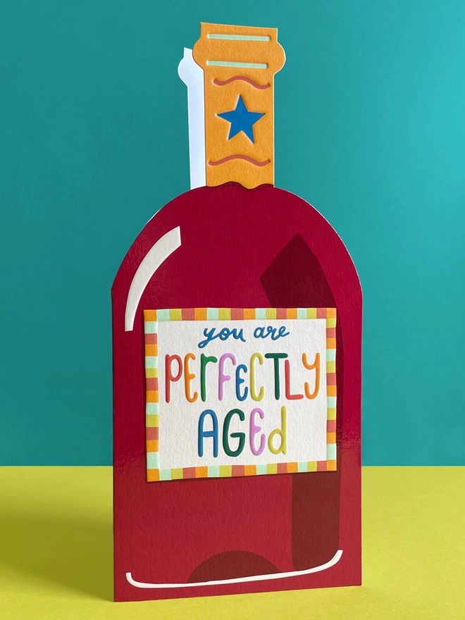  A vibrant die cut birthday card in the shape of a wine bottle with a rainbow coloured ‘You are perfectly aged’ message