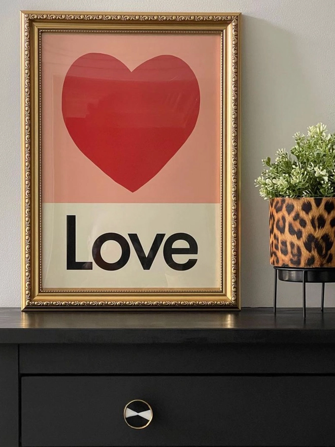 framed illustrated love heart wall print with the word Love at the bottom propped on top of drawers