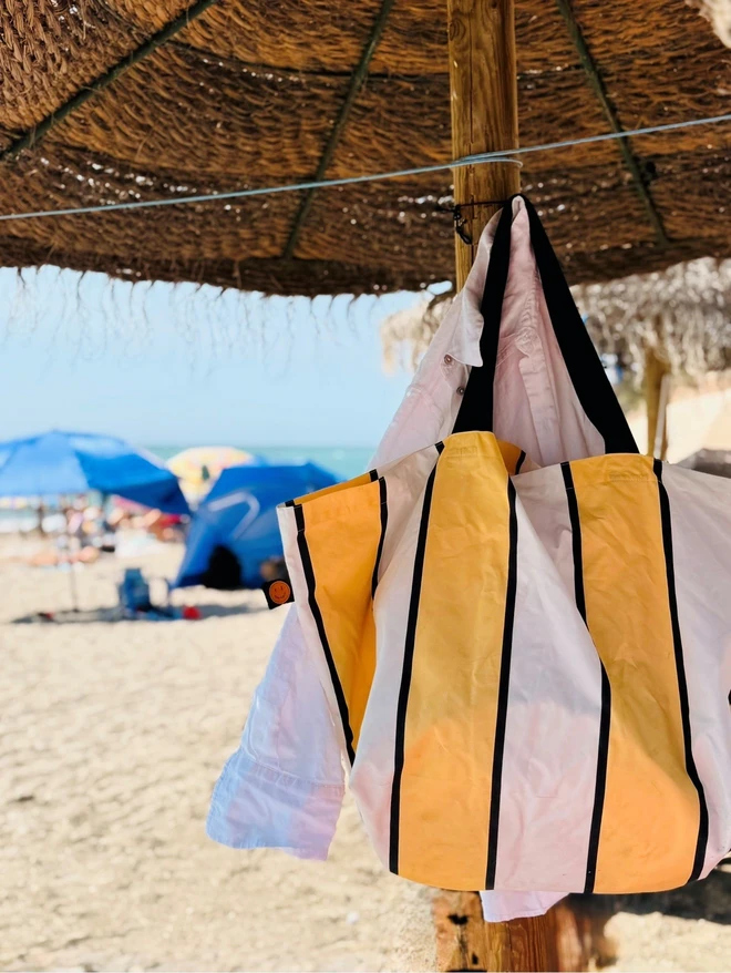 yellow and white stripe beach bag hanging under sun shade