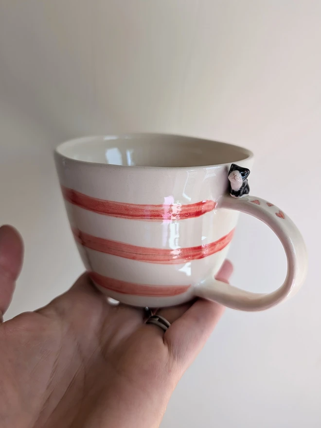 pottery cup with red stripes, hearts and a ceramic black and white cat on the handle