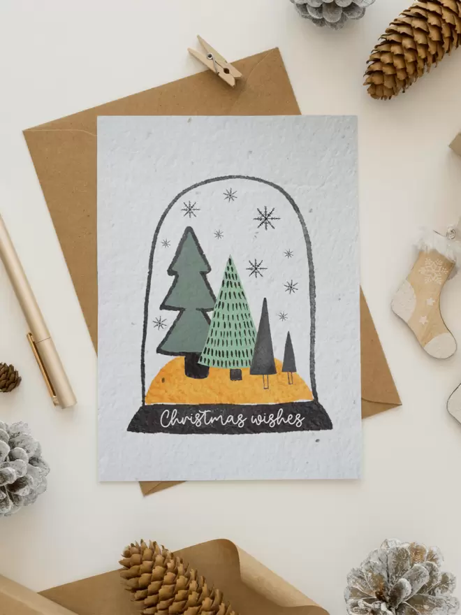 In the centre of the image is a card with an illustrated snow globe with trees in it with the writing 'Christmas Wishes' underneath surrounded by Christmas themes items