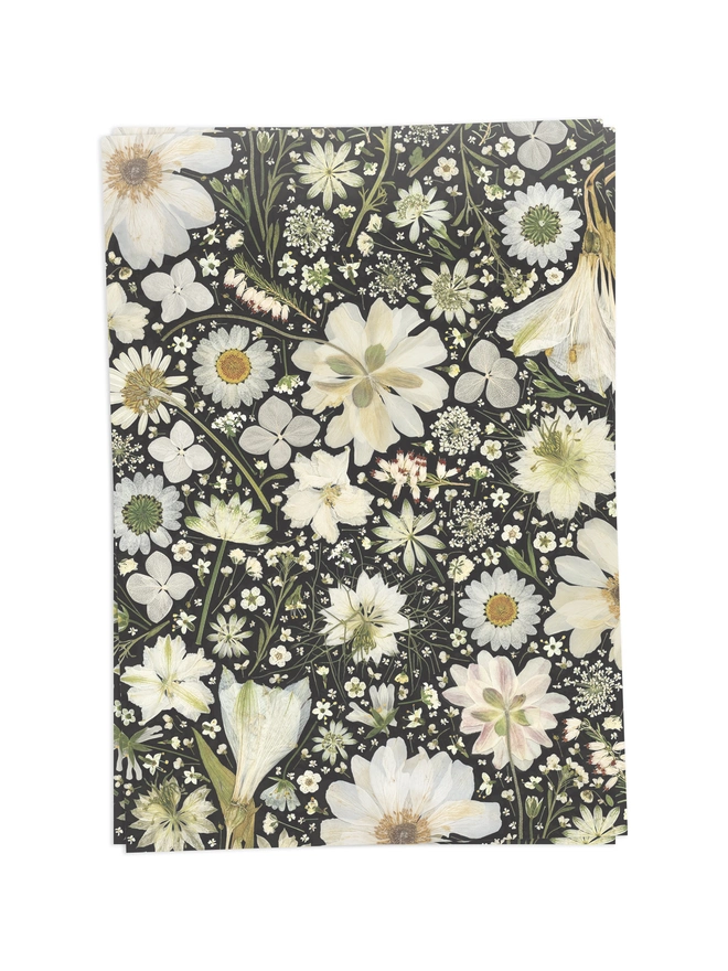 2 Folded wrapping paper sheets with a floral design created from pressed white flowers on a black background.