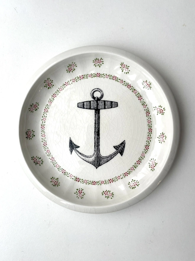 vintage plate with an ornate border, with a printed vintage illustration of an ship's anchor in the middle 