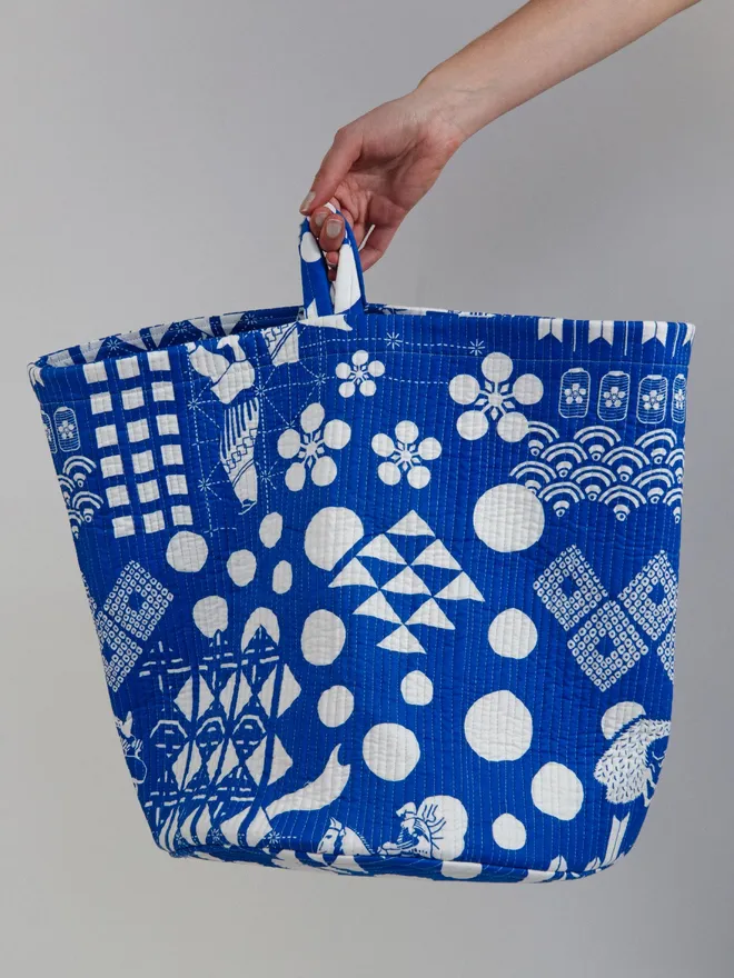 Blue Festival Quilted Storage Basket, a person holding a blue basket against a grey backdrop. 