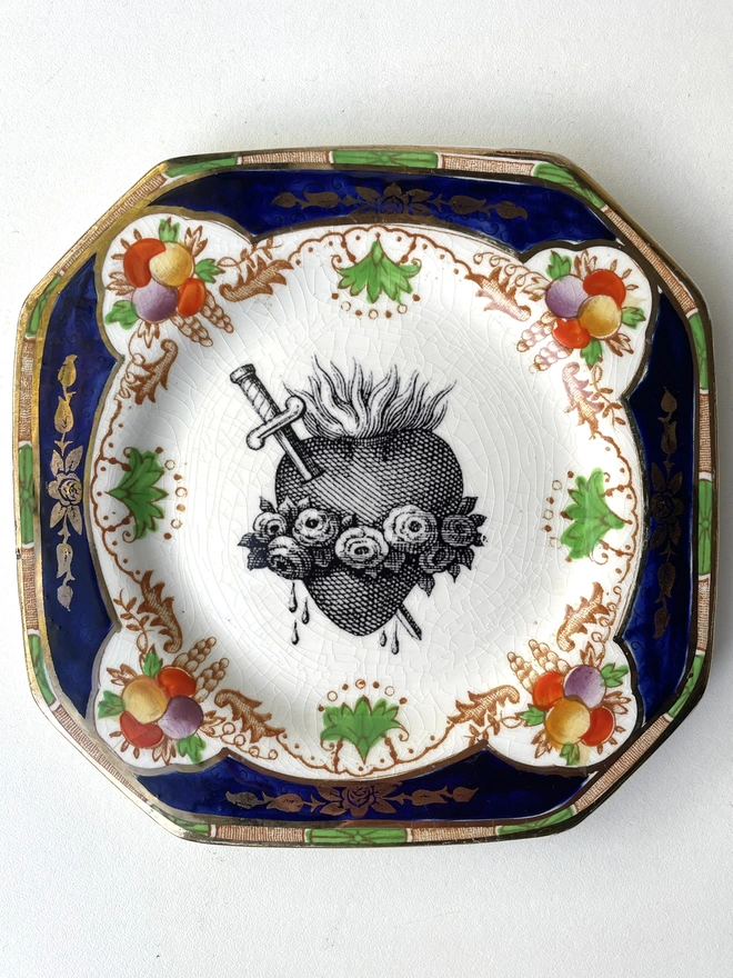 a vintage plate with an ornate border,  printed on that is a black illustration of a sacred heart