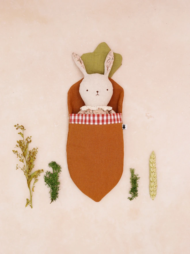 Handmade linen bunny doll in pink floral outfit and frilly lace colour, in a carrot shaped sleeping bag made with linen and gingham cotton. 