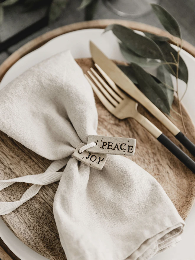 Two ceramic tags with the wording 'peace' and 'joy' tied to a napkin on a beautiful place setting