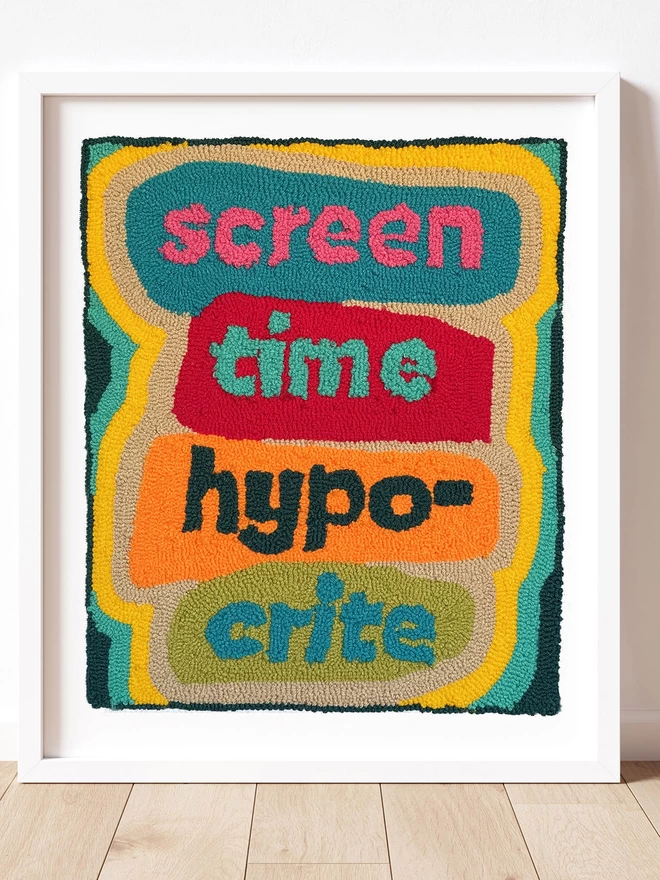 Screen Time Hypocrite written in bright wool on coloured block in a white box frame on a wooden floor