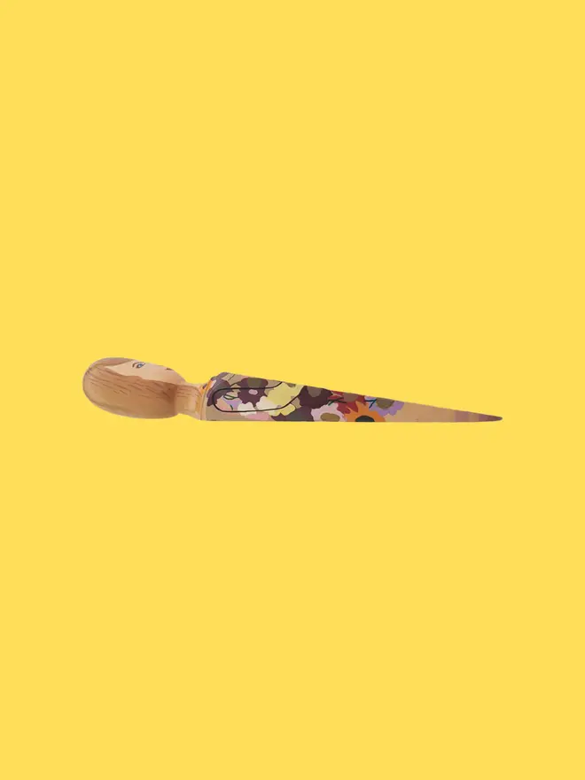 Wooden Door Stopper (Swifty Floral Outfit), a colourful wooden door stop sitting on a yellow surface. 
