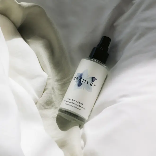 White spray bottle with black lid, lying on a pile of white cloth/bedding