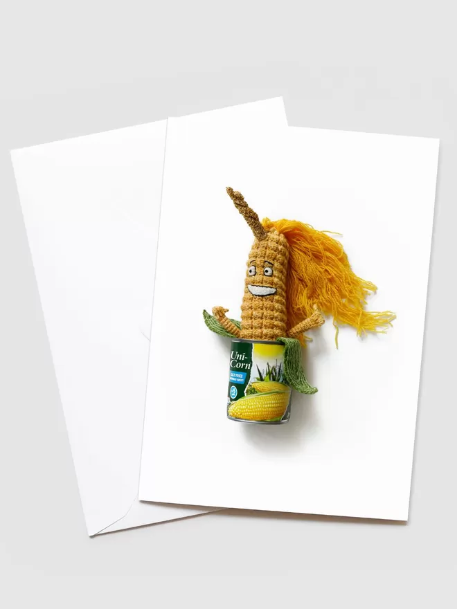 Kate Jenkins Uni-Corn Card seen with a white envelope. A hand crotched corn with a unicorn horn is seen in a tin corn can.