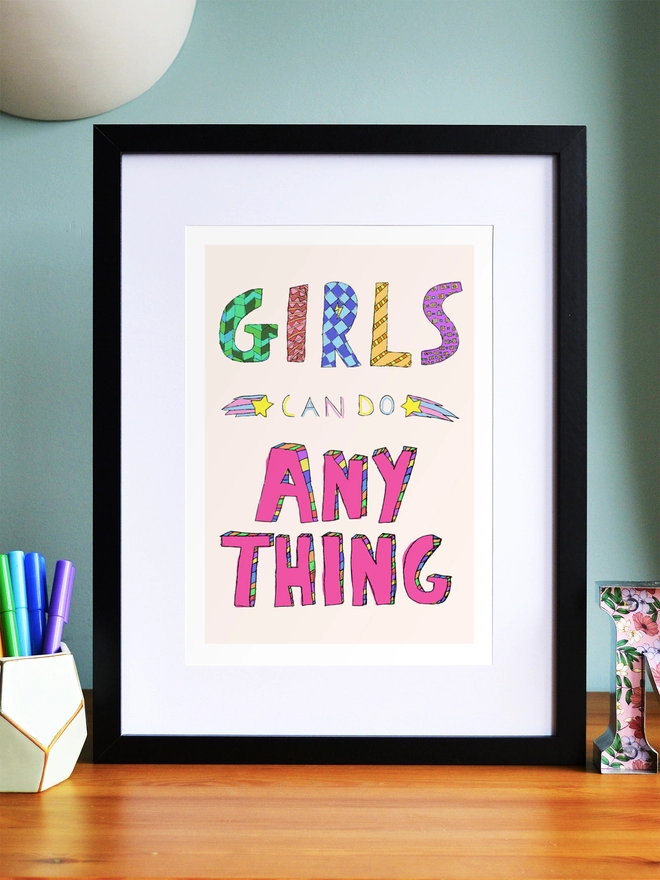 Art print saying 'Girls can do anything' in a black frame in a child's room