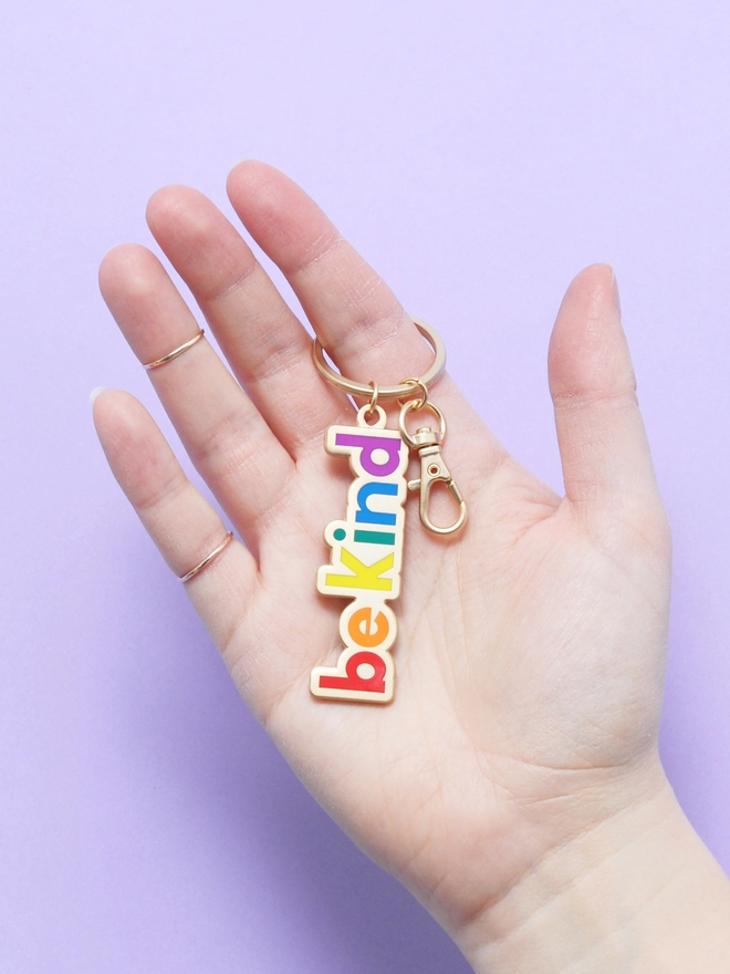 Hand holding Enamel keyring with 'Be Kind' design in rainbow colours