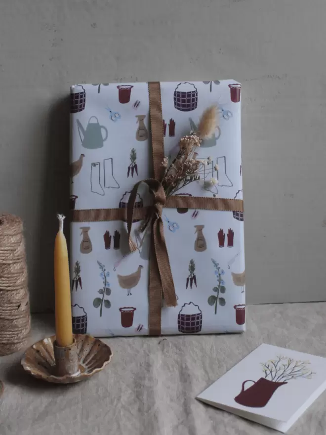 gardening wrapping paper and ribbon, next to candle and card with mimosa on. 