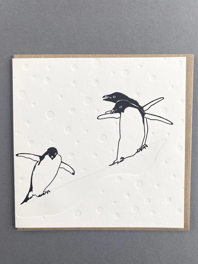Full image of three penguins sliding down a snowy hill