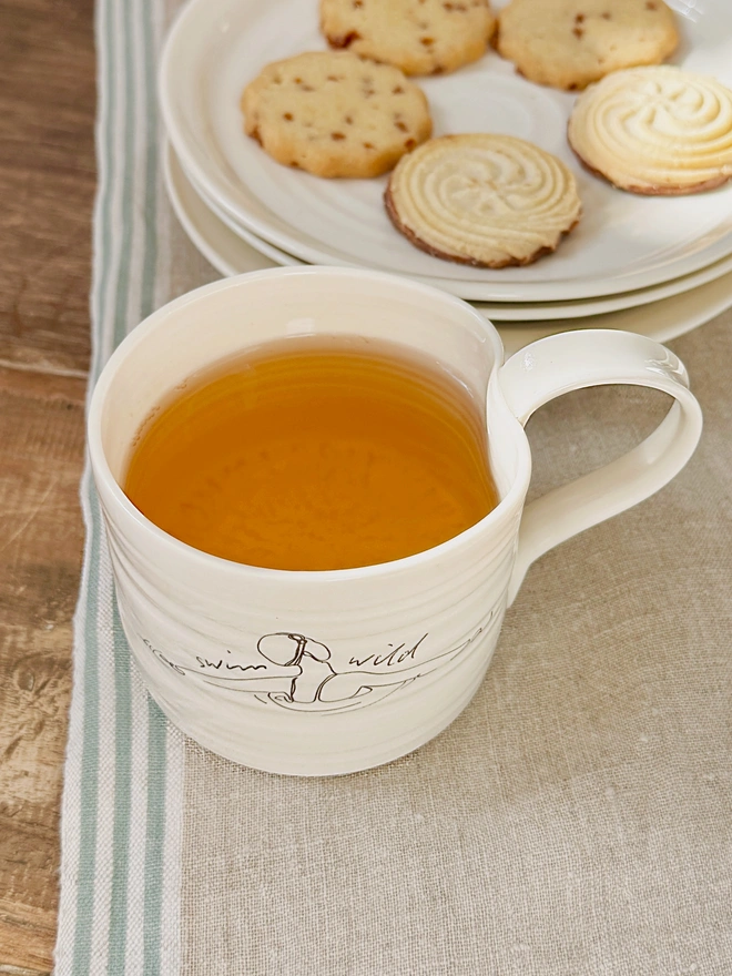 Handcrafted porcelain ‘Swim Wild’ mug – unique ceramic coffee cup for swimmers, nature lovers, and outdoor adventurers.