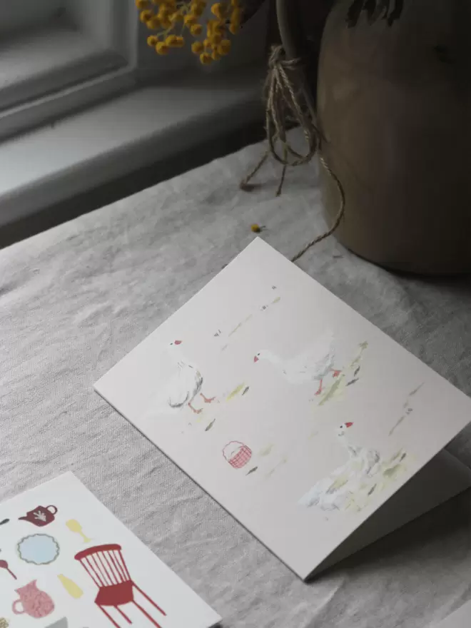 a card with geese on next to a vase of mimosa