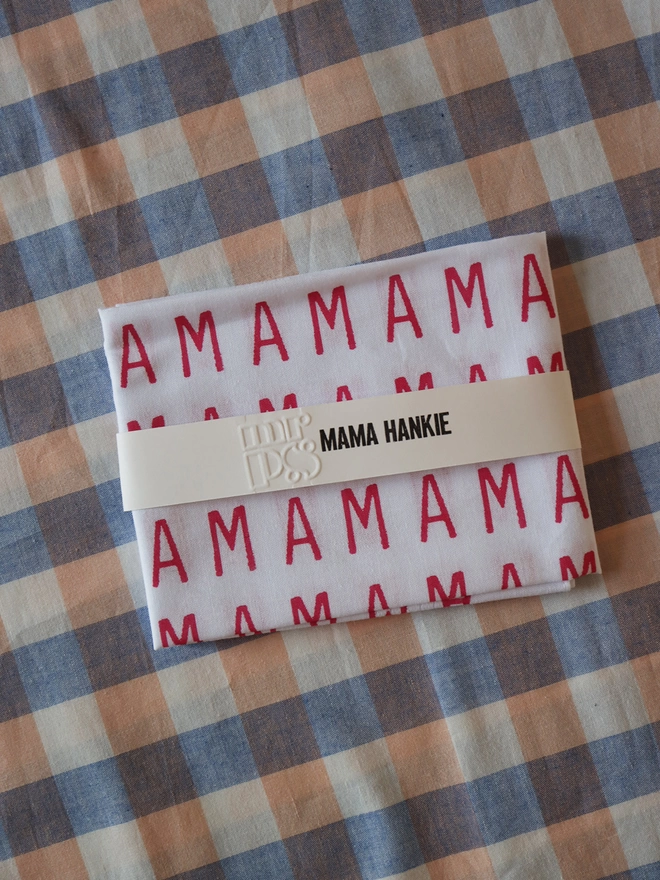 A folded Mr.PS MAMA Hankie on a gingham tablecloth