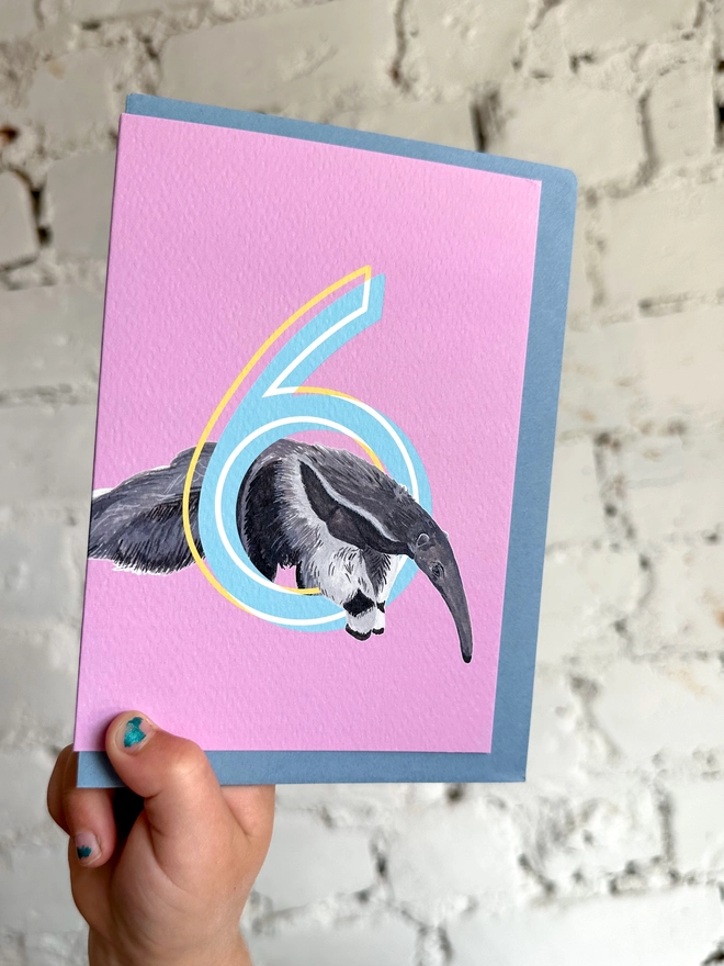 a pink card featuring a big blue number 6 and a giant anteater illustration with a blue envelope