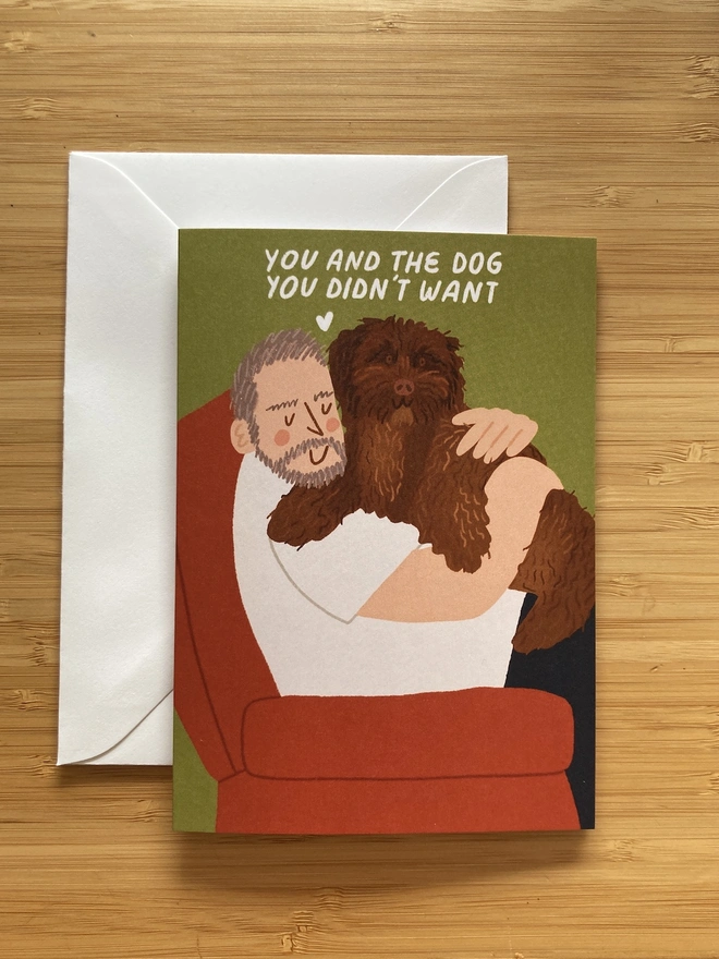 Illustrated greetings card of a dad cuddling a cockapoo dog. The text says 'you and the dog you didn't want'