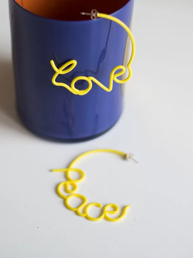 Love and Peace Yellow large earrings seen on a blue cup.