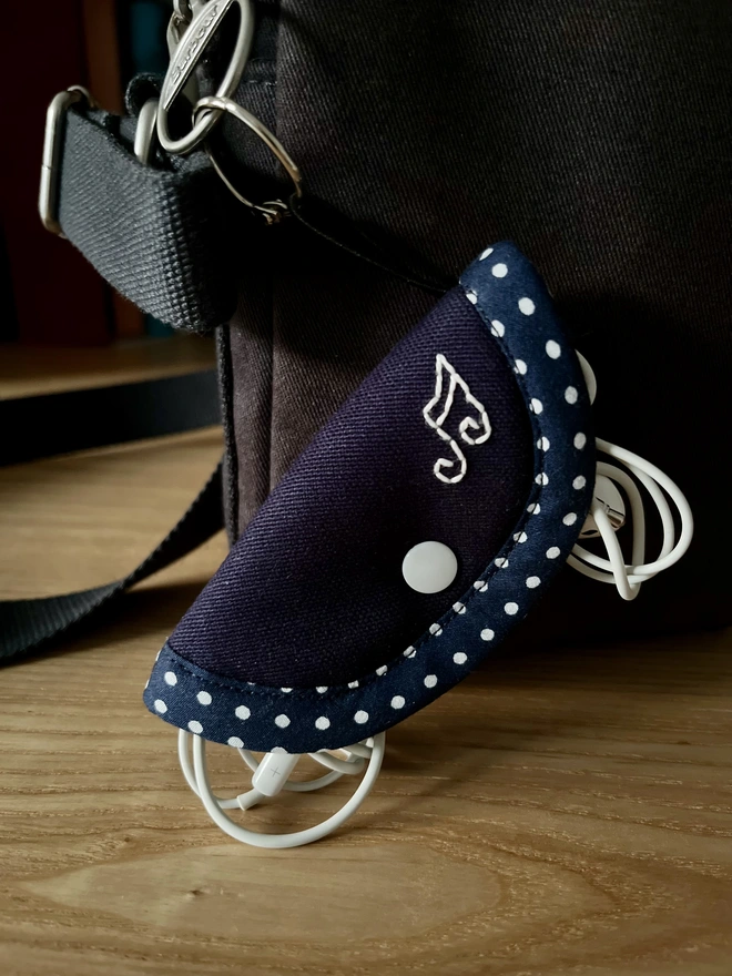 Soft navy polka dot earphone case embroidered with musical notes, attached to bag.