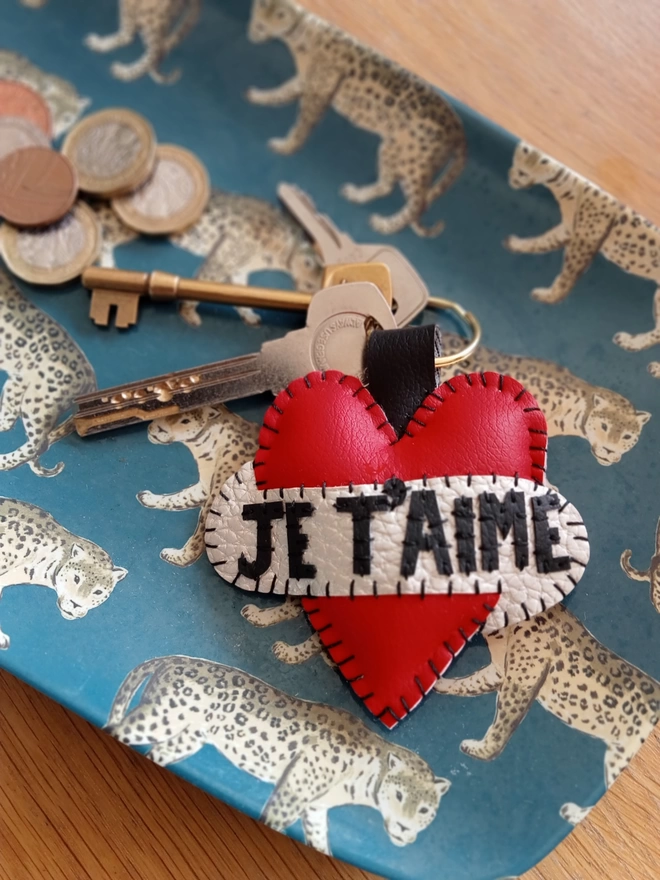 A red leatherette heart keyring, with black lettering spelling Je T'aime across a white scroll