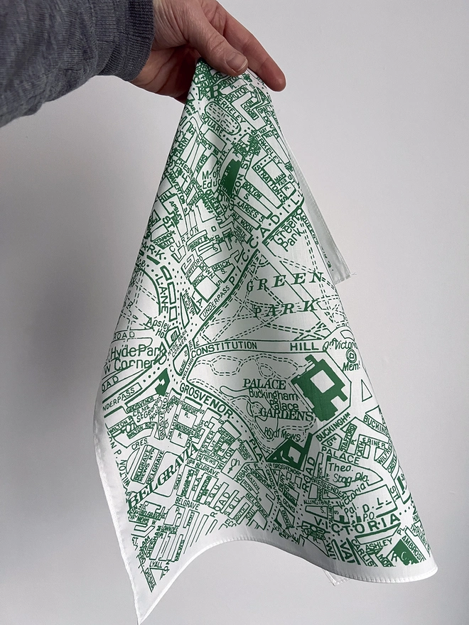 A white hand holding a green London Piccadilly Map Handkerchief against a wall
