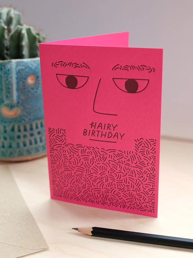 Bright pink letterpress printed bearded man card on shelf.