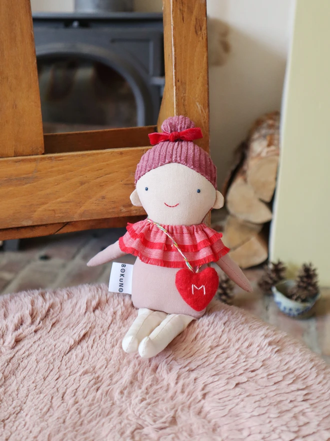 Handmade cloth doll with a pink corduroy hair with a red velvet bow and a layered red ruffle collar and pink outfit, wearing a small red felt heart bag with the letter “M”