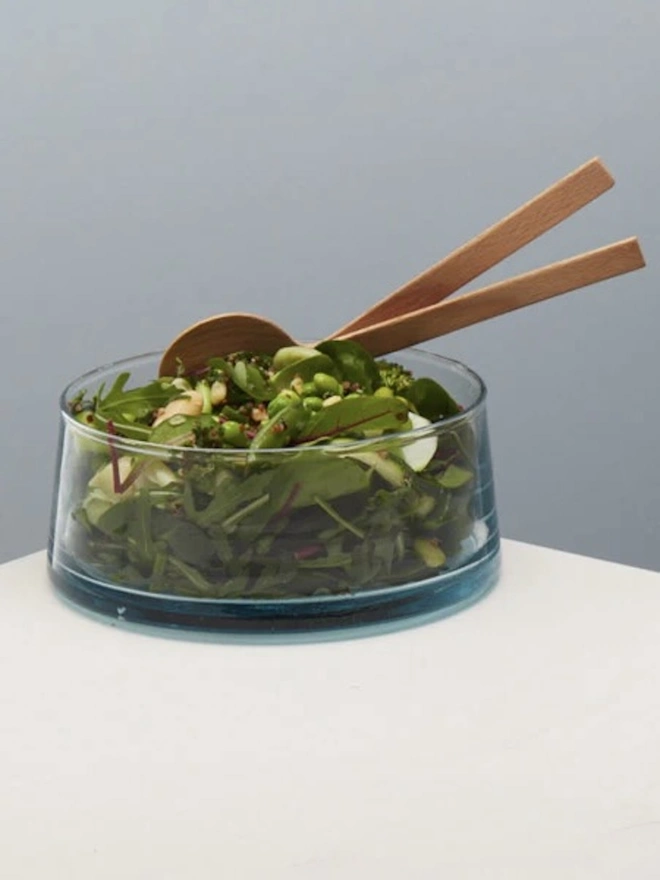 Low Glass Dish, a small glass dish sitting on a white counter top against a baby blue backdrop. It is filled by a salad. 