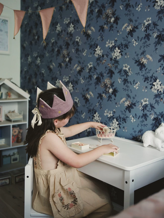 Girl in her lilac star embroidered crown playing with her toys at a table