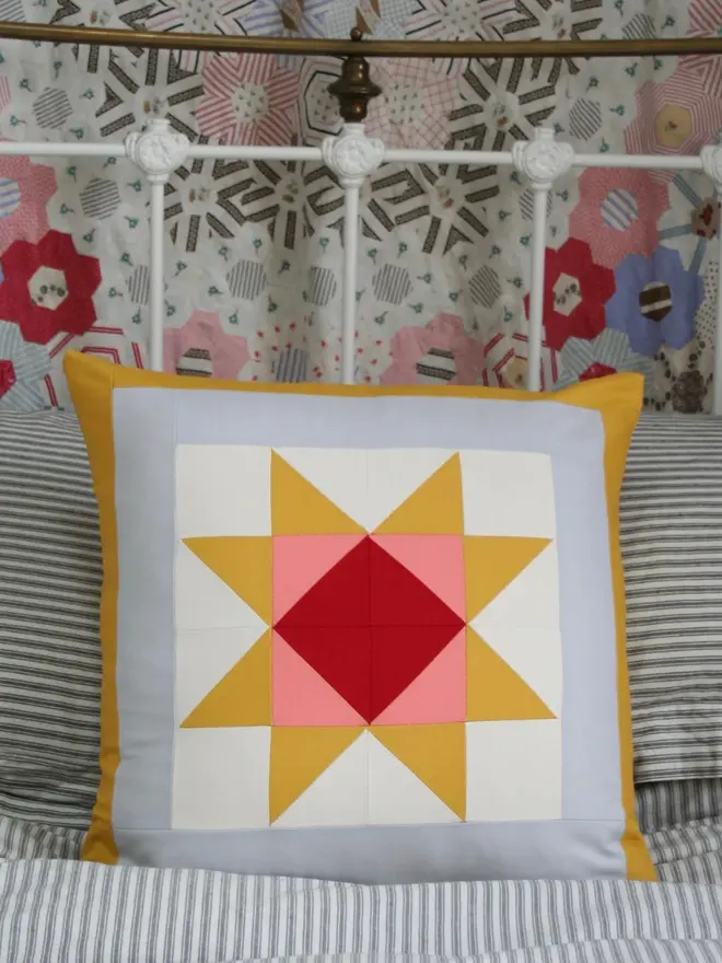 Warm Hearth Patchwork Cushion, on a bed. 