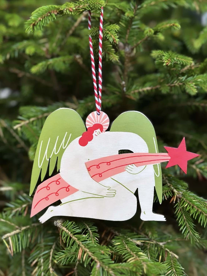 A wooden, handprinted angel holding a star, hangs on a green christmas tree