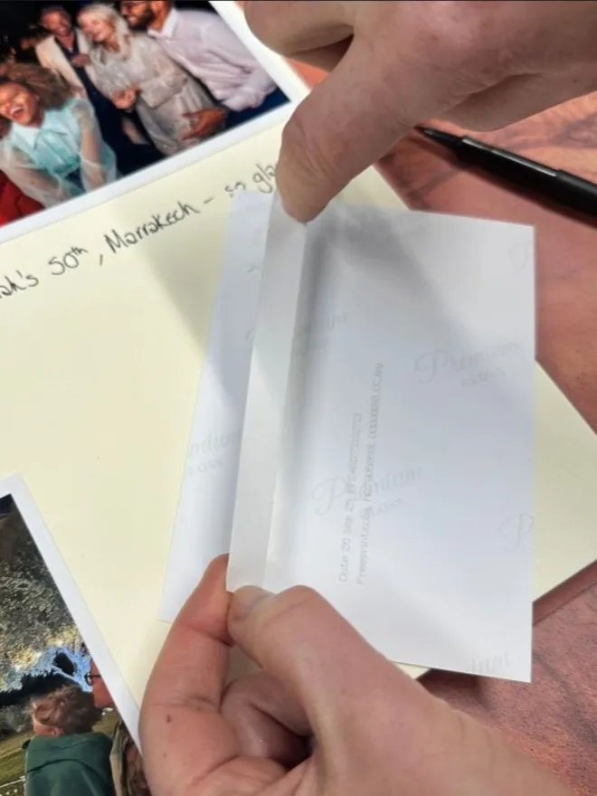 A piece of double-sided mounting tape is being applied to the back of a photo before being stuck into an open photo album.