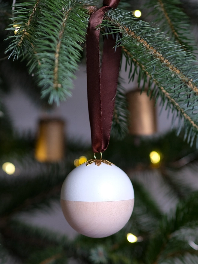Wooden and white Christmas gift bauble with a removable lid, hanging from a Christmas tree with a space inside for a handwritten message, gift or surprise