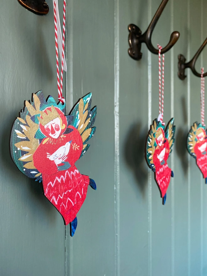 Red and green illustrated angel decoration by Esther Kent, hanging against a green background