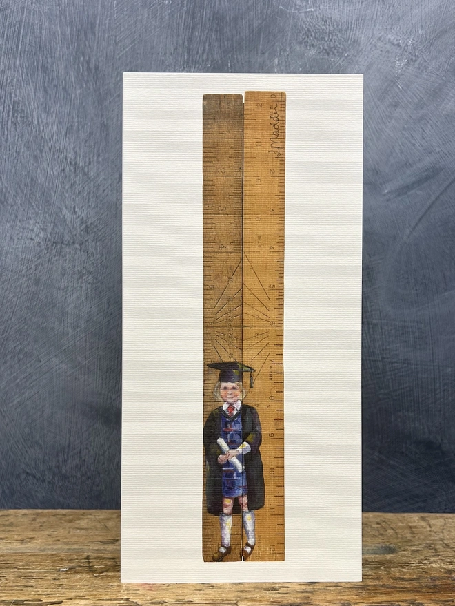 little girl wearing graduation cap and gown standing in front of school rulers