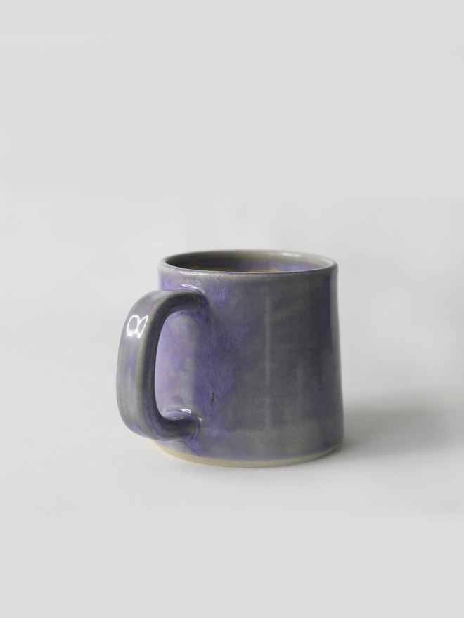 A handmade ceramic standard mug in glossy amethyst purple glaze with a chunky loop handle, photographed against a plain light grey background