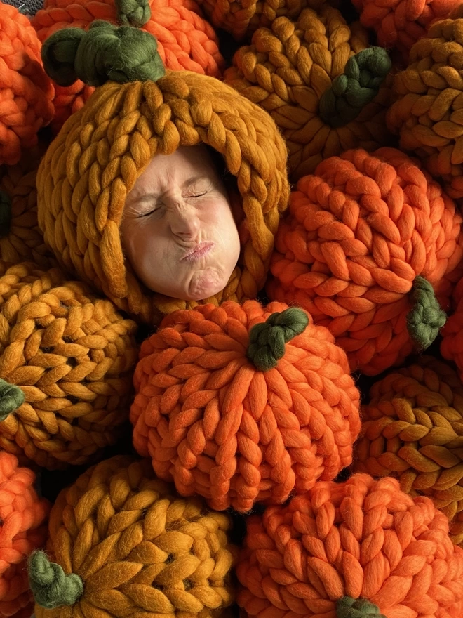 A pile of orange pumpkins seen with a person wearing the hat 