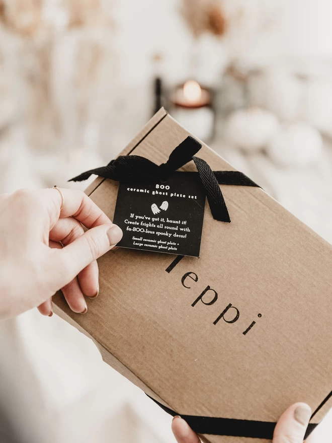 hands holding a brown gift box, tied with black ribbon and a foiled tag