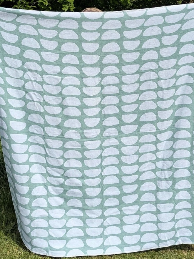 Organic Cotton Throw, a person holding the throw in front of them outside. 