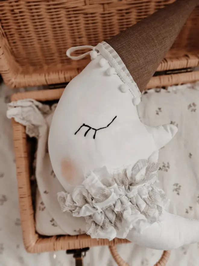 Hanging Moon Pillow Decoration, a hanging moon pillow decoration sitting in a wooden hamper amongst other bed accessories. 