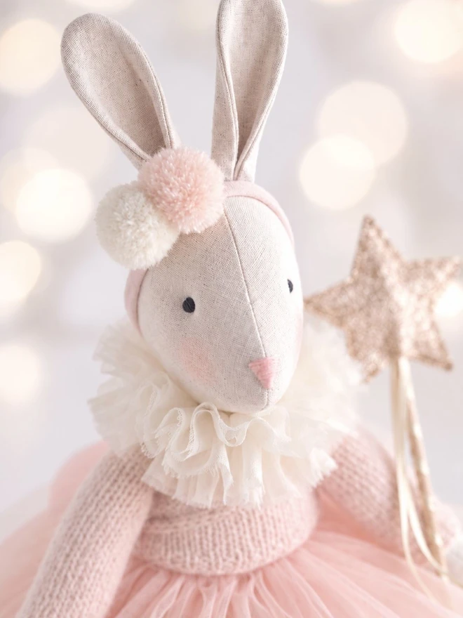 Close-up of Verity Isabelle ballerina bunny wearing a full ivory ruffle collar, pale pink outfit and holding a gold star wand.