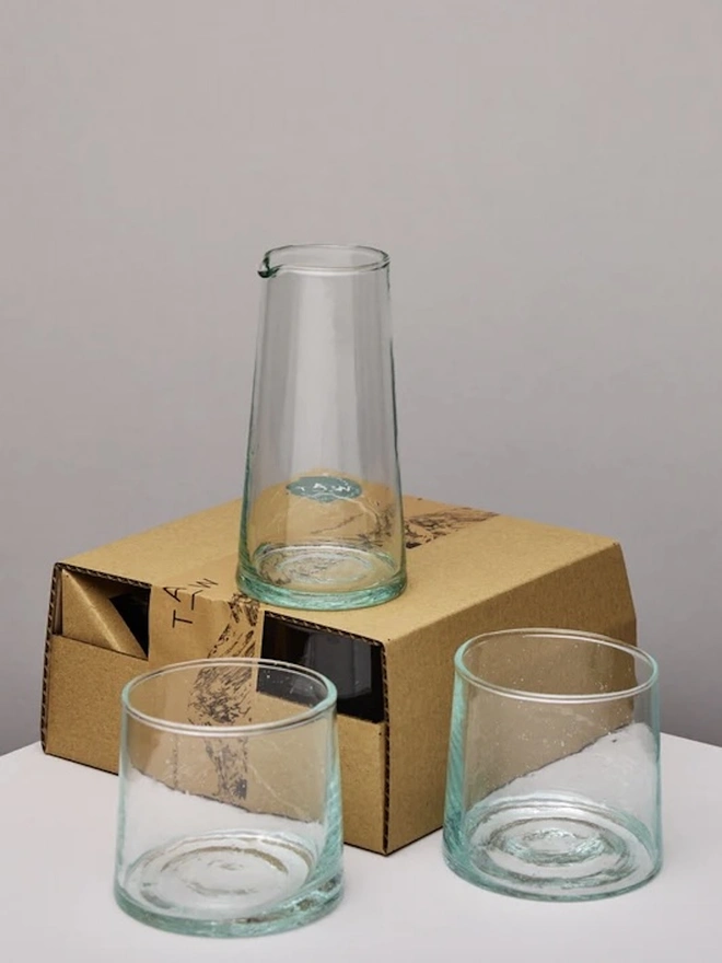 Whisky Glasses (Set Of 3), a set of whisky glasses and a jug sitting on top of a packaging box against a grey backdrop. 