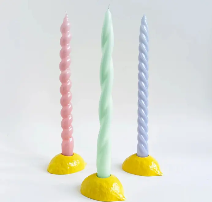 Lemon Candlestick Holder. Three pastel candles placed in three yellow lemon candlestick holders against a white background. 